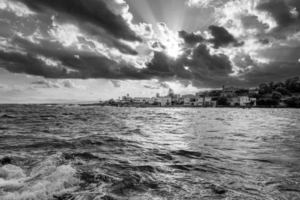 Black and white shot of sun\'s rays break through thick clouds illuminating the wavy stormy sea.