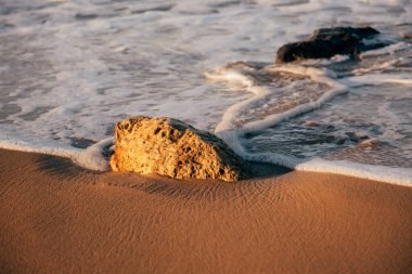 Deniz, dalgalar, sahil, gün batımında kum ve taş.