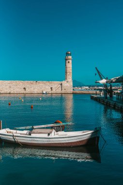 Sıcak bir kış gününde yakalanan eski deniz feneri ve bir tekne. Su sakin ve güzel yansımaları var..