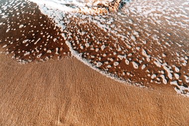 Gün batımında kıyıya vuran dalgaların tam üstünde. Taş, dalga, köpük.