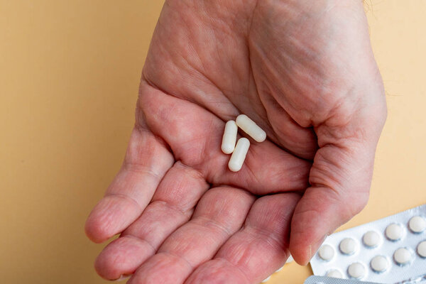 Male hand holding three capsules with medicine, vitamins or sports supplement in hand on yellow background. Close up of Vitamin D pills in blister packs on yellow background.