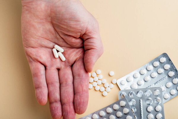 Male hand holding three capsules with medicine, vitamins or sports supplement in hand on yellow background. Close up of Vitamin D pills in blister packs on yellow background.