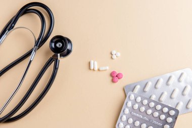 Siyah ve çelik fonendoskop, sarı arka planda haplar..