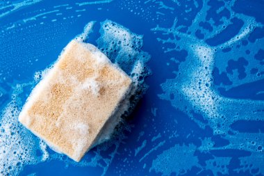 Bulaşık yıkamak için köpük sünger. Fotokopi alanı olan mavi seramik masa. Islak yüzeyde temizlik süngeri