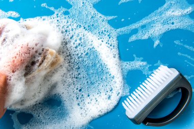 El temizleme süngerini tutar ve mavi bir fayansa sabunlu köpük siler. mavi arka plan. Temizlik konsepti, temizlik hizmeti. Pankart. Düz yatış, üst görünüm