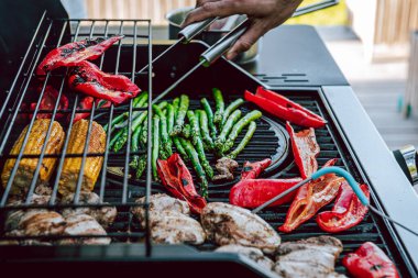 Izgara tavuk, mısır koçanı, kırmızı biber ve sıcaklığı kontrol eden kuşkonmaz, insan ellerinde et maşası..