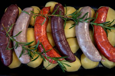 Raw sausages in the oven. Close-up of bowl with raw homemade blood sausage, pork sausage and chorizo in oven with potatoes. homemade traditional food. clipart