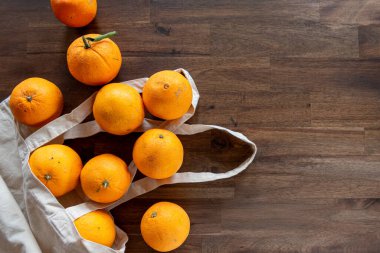 Kahverengi masadaki, yeniden kullanılabilir doğa çantasına yerleştirilmiş taze soyulmamış portakalların üst görünümü.