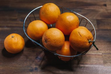 olgun soyulmamış portakallar kahverengi ahşap bir masada meyve sepetinde