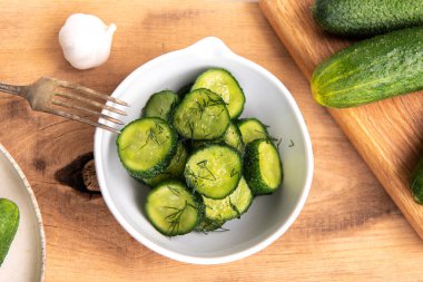 Ahşap bir masada seramik beyaz bir kasede organik salatalıklar dilimler. Taze sebze ve dereotu, ahşap dokuma masasında sarımsak. Salata..