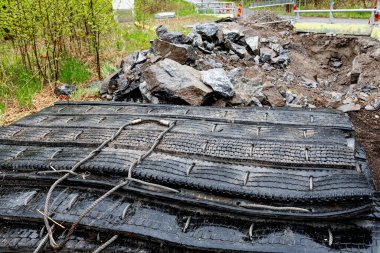 Ormanda bir yol inşaatı ya da bakım alanı, güvenlik bariyerleri ve kayalar ve enkazlarla dolu büyük bir delik. Çevreleyen ağaçlar ilkbahar yapraklarında..