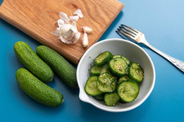 İnce dilimlenmiş salatalık salatası taze dereotu ve susam tohumlarıyla süslenmiş, mavi arka planda beyaz bir kasede servis ediliyor. Hafif, sağlıklı ve ferahlatıcı..
