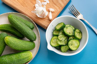 İnce dilimlenmiş salatalık salatası taze dereotu ve susam tohumlarıyla süslenmiş, mavi arka planda beyaz bir kasede servis ediliyor. Hafif, sağlıklı ve ferahlatıcı..