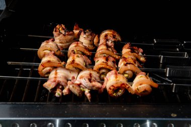 Sulu domuz eti dilimleri sarılmış ve şiş vaziyette açık havada ızgara pişiriliyor. Yaz barbeküsü, açık hava yemekleri ve geleneksel ev yapımı yemek kavramları için mükemmel..