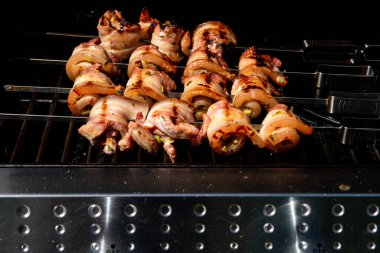 Sulu domuz eti dilimleri sarılmış ve şiş vaziyette açık havada ızgara pişiriliyor. Yaz barbeküsü, açık hava yemekleri ve geleneksel ev yapımı yemek kavramları için mükemmel..