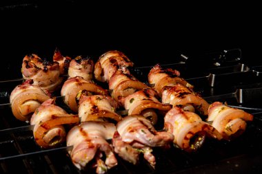 Sulu domuz eti dilimleri sarılmış ve şiş vaziyette açık havada ızgara pişiriliyor. Yaz barbeküsü, açık hava yemekleri ve geleneksel ev yapımı yemek kavramları için mükemmel..