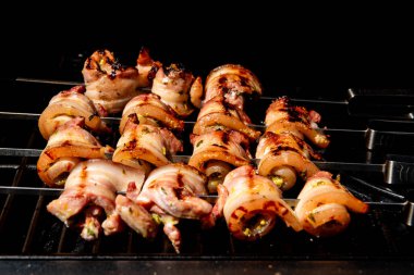 Sulu domuz eti dilimleri sarılmış ve şiş vaziyette açık havada ızgara pişiriliyor. Yaz barbeküsü, açık hava yemekleri ve geleneksel ev yapımı yemek kavramları için mükemmel..