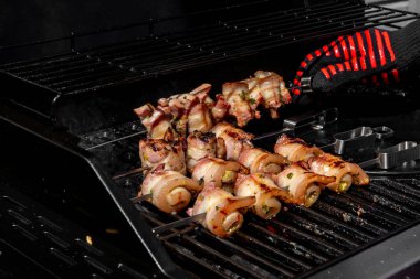 Sulu domuz eti dilimleri sarılmış ve şiş vaziyette açık havada ızgara pişiriliyor. Yaz barbeküsü, açık hava yemekleri ve geleneksel ev yapımı yemek kavramları için mükemmel..