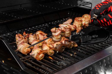 Sulu domuz eti dilimleri sarılmış ve şiş vaziyette açık havada ızgara pişiriliyor. Yaz barbeküsü, açık hava yemekleri ve geleneksel ev yapımı yemek kavramları için mükemmel..