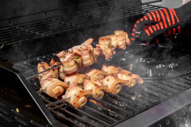 Sulu domuz eti dilimleri sarılmış ve şiş vaziyette açık havada ızgara pişiriliyor. Yaz barbeküsü, açık hava yemekleri ve geleneksel ev yapımı yemek kavramları için mükemmel..