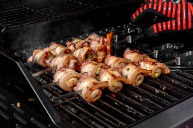 Sulu domuz eti dilimleri sarılmış ve şiş vaziyette açık havada ızgara pişiriliyor. Yaz barbeküsü, açık hava yemekleri ve geleneksel ev yapımı yemek kavramları için mükemmel..