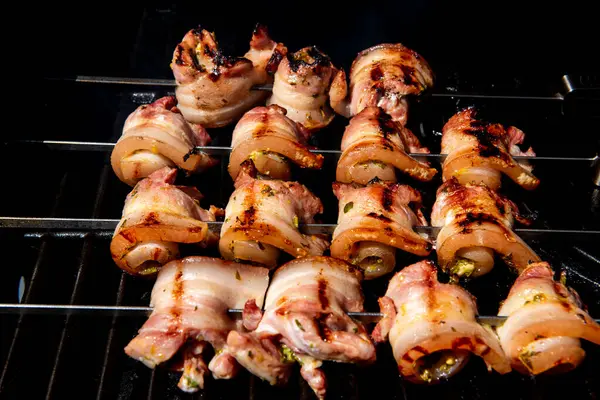 Sulu domuz eti dilimleri sarılmış ve şiş vaziyette açık havada ızgara pişiriliyor. Yaz barbeküsü, açık hava yemekleri ve geleneksel ev yapımı yemek kavramları için mükemmel..