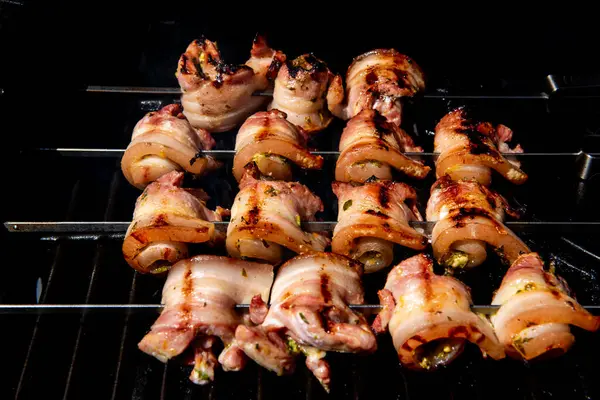 Sulu domuz eti dilimleri sarılmış ve şiş vaziyette açık havada ızgara pişiriliyor. Yaz barbeküsü, açık hava yemekleri ve geleneksel ev yapımı yemek kavramları için mükemmel..