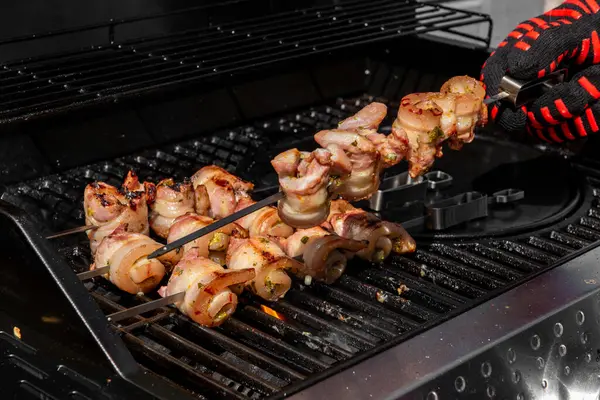 Sulu domuz eti dilimleri sarılmış ve şiş vaziyette açık havada ızgara pişiriliyor. Yaz barbeküsü, açık hava yemekleri ve geleneksel ev yapımı yemek kavramları için mükemmel..