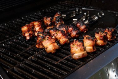 Sulu domuz eti dilimleri sarılmış ve şiş vaziyette açık havada ızgara pişiriliyor. Yaz barbeküsü, açık hava yemekleri ve geleneksel ev yapımı yemek kavramları için mükemmel..