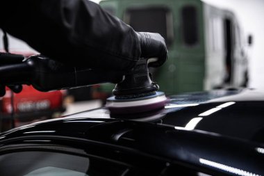 Stüdyonun çalışanı arabanın siyah boyasını elektrikli cilalama makinesiyle parlatıyor.