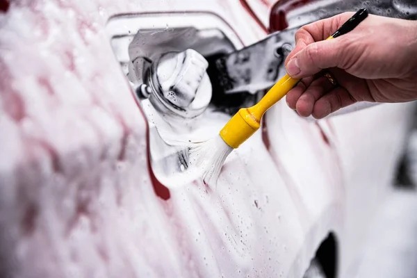 employee of the car detailing studio washes the area around the fuel filler with a brush