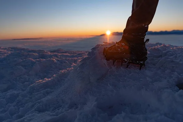 Man climbs a mountain peak in winter during sunrise. A shoe with spikes on - crampons. Sunrise on Babia Gora with a view of the Tatra Mountains