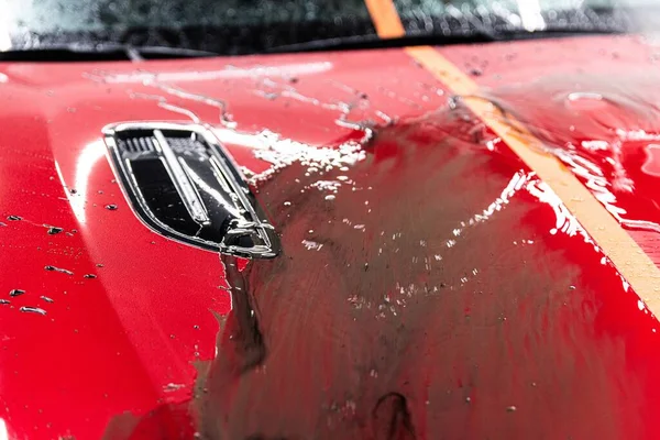 Rinsing dirt from the paint of a red car with a touchless pressure washer