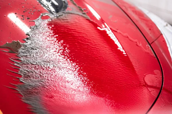 Rinsing dirt from the paint of a red car with a touchless pressure washer