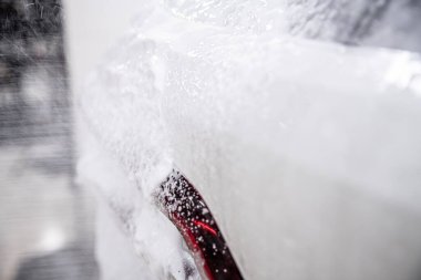 White active foam covering the paintwork of a white car at a car wash