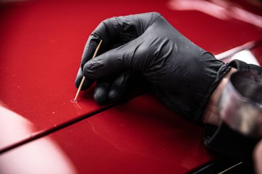 Employe of car paint shop or car detailing studio performs a paint touch-up on a red car