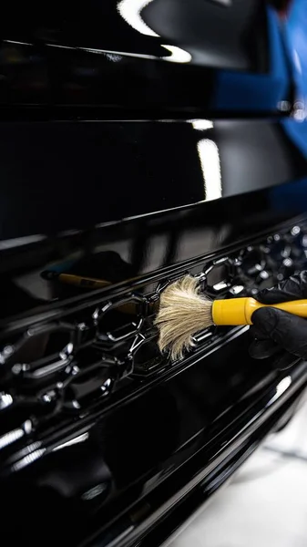 employee of a car detailing studio or a car wash thoroughly cleans a car element with a brush
