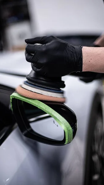 スタジオ又は洗車場を詳述した車の従業員は バックミラーの近くの黒い車の塗装を磨く — ストック写真