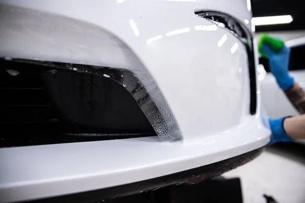 详细的汽车工作室员工 一个包装 正在保护一个白色汽车保险杠与无色的保护Ppf膜 Ppf膜保护油漆不受划伤和损坏 图库图片