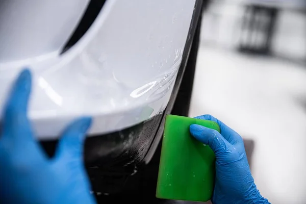 详细的汽车工作室员工 一个包装 正在保护一个白色汽车保险杠与无色的保护Ppf膜 Ppf膜保护油漆不受划伤和损坏 免版税图库照片