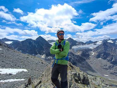 Schrankogel yürüyüşü sırasında Avusturya 'daki Tyrol dağlarında bir adam. Yeşil bir ön cam, yağmura dayanıklı bir ceket ve beyaz bir kask giymişti. Spor güneş gözlüğü takıyor..