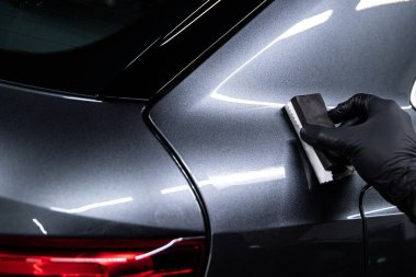 Araba temizleme ya da araba yıkama işçisi gümüş araba gövdesine seramik kaplama uyguluyor. 