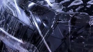 Araba temizleme stüdyosunun çalışanları siyah bir arabanın kaputuna temiz bir koruyucu PPF filmi uyguluyorlar. Video, titiz bir şekilde yüksek kalitede koruma ve bitirme sürecini gösteriyor..