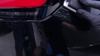 Araba temizleme stüdyosu çalışanı seramik kaplama uyguluyor, kaplamayı aplikatörün üzerine dökerek başlıyor. Video titiz süreci ve detaylara olan dikkati vurguluyor