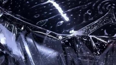 Araba temizleme stüdyosunun çalışanları siyah bir arabanın kaputuna temiz bir koruyucu PPF filmi uyguluyorlar. Video, titiz bir şekilde yüksek kalitede koruma ve bitirme sürecini gösteriyor..