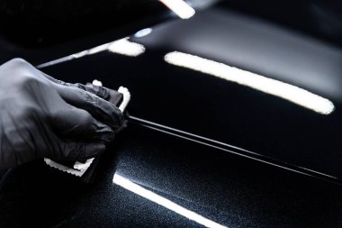 Araba yıkama ya da stüdyo çalışanı, koyu parlatıcı ve gelişmiş koruma sağlayan siyah araba boyasına seramik ya da grafen kaplama uygular.