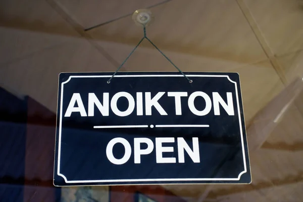 Open sign in Greek and English languages hanging on the door of a shop in Greece