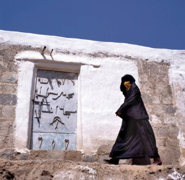 Peçeli Müslüman bir kadın Sanaa caddesinde yürüyor, Yemen. Arka planda tipik bir Yemen evinin kapısı var..