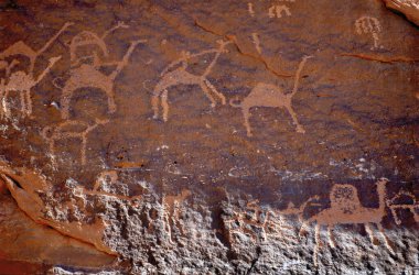 Ürdün 'ün Wadi Rum kentindeki kırmızı kumtaşı kayalarının yüzeyinde göçebe bedeviler tarafından yapılan tarih öncesi taş yazıtların ve taşların ön yüzünü kapatın. Develeri betimleyen figürler 