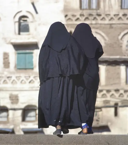 两名身穿黑色布卡的妇女走在也门首都萨那的一条街上 图库照片